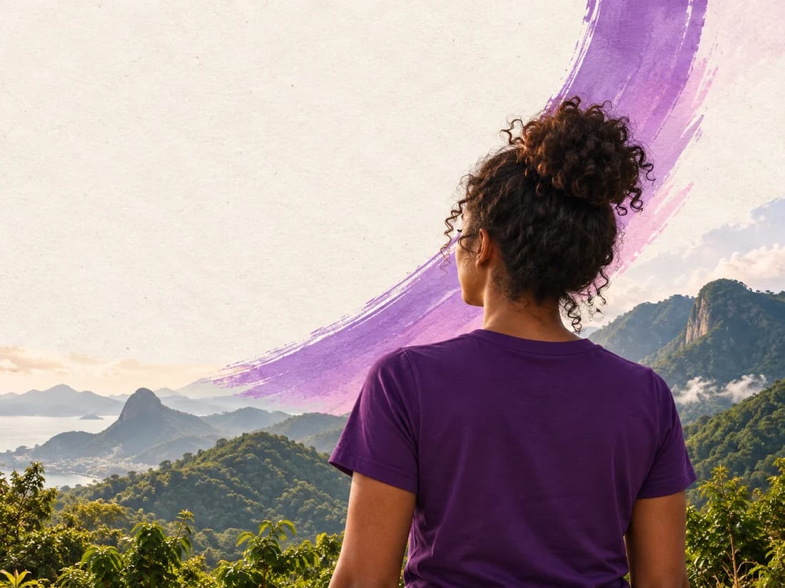 Mulher de camiseta roxa vista de costas, olhando para uma paisagem de montanhas